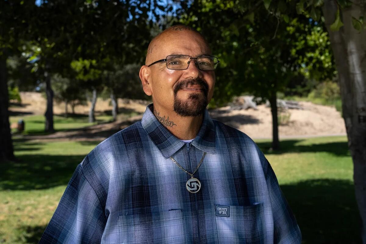 Cheech Raygoza wearing a flannel smiling posing for a picture in front of a tree