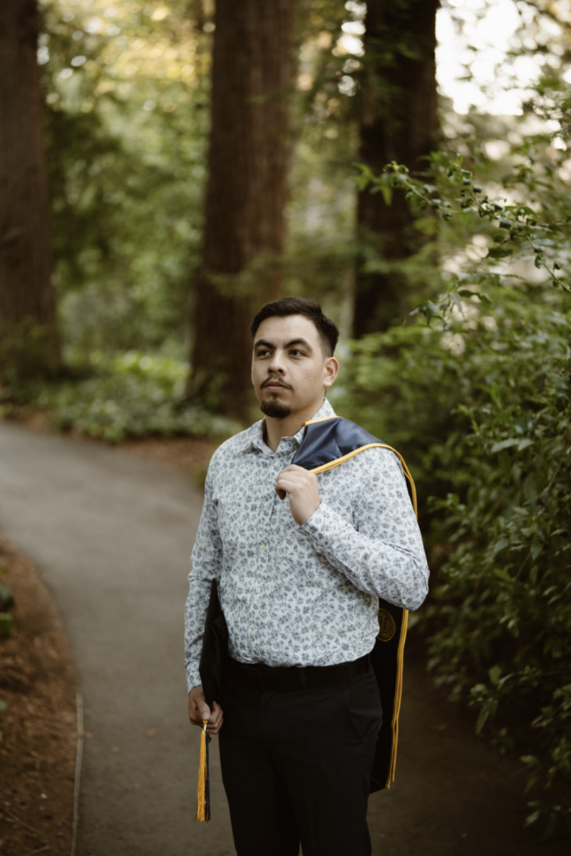 Pedro Rodriguez wearing professional attire with his graduation sole handing from his shoulder in front of trees